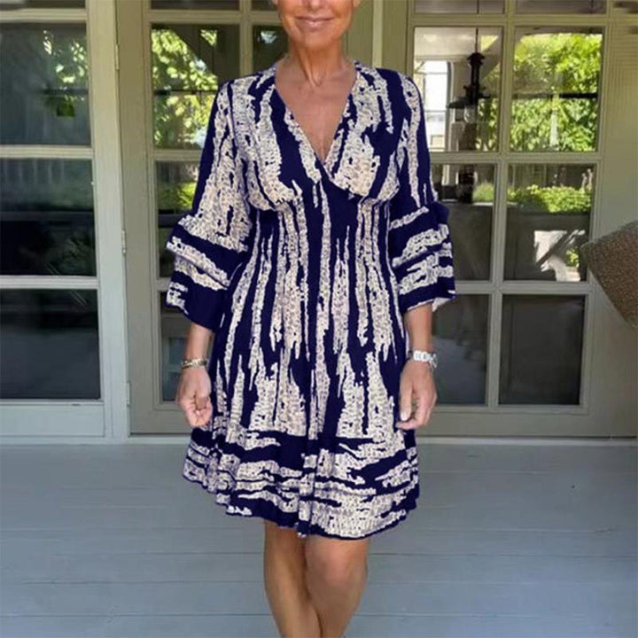 Vrouw in marineblauwe jurk met abstract patroon, driekwart mouwen, voor glazen deuren. Zomerse mode, casual stijl, comfortabele pasvorm.