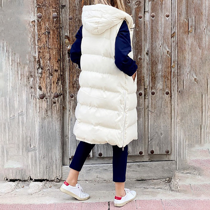 Vrouw in lange, witte gewatteerde bodywarmer met capuchon, blauwe mouwen, voor houten deur. Wintermode, casual outfit, trendy dameskleding.