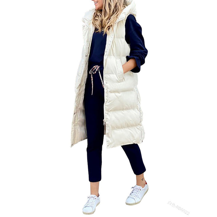 Vrouw in lange off-white gewatteerde bodywarmer, donkerblauwe trui en broek, witte sneakers. Modieuze winteroutfit, casual dameskleding.