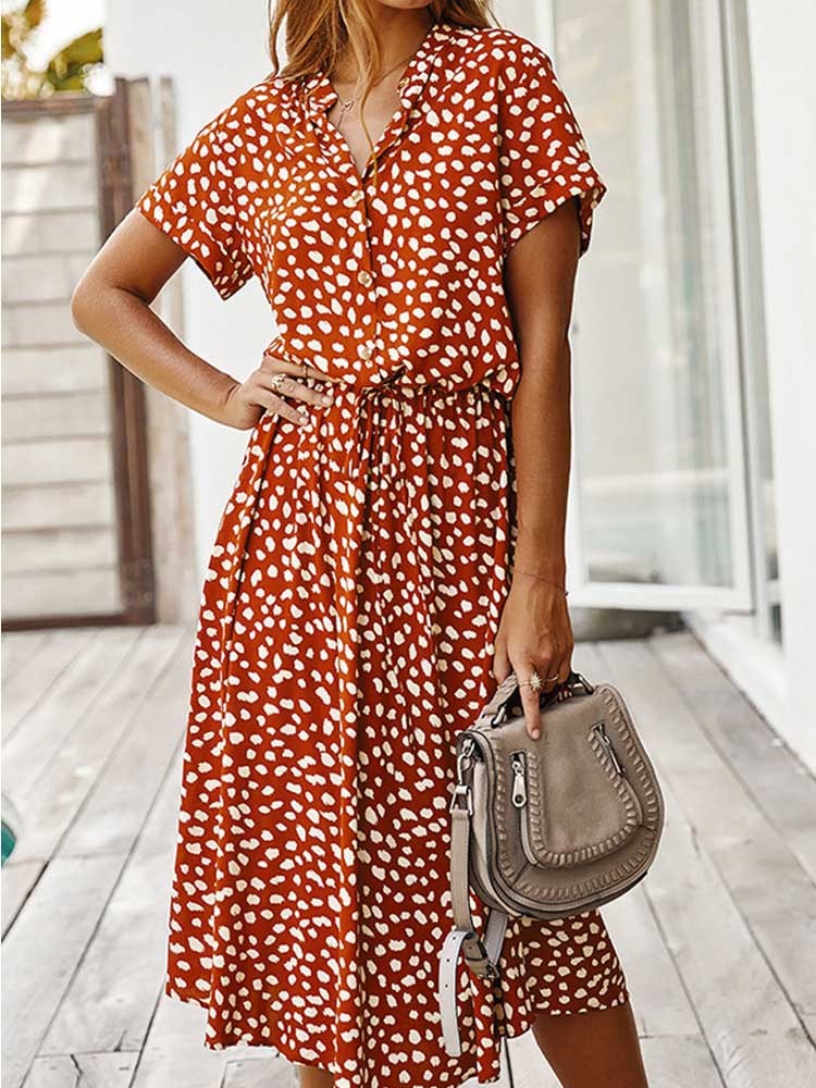 Vrouw in oranje-witte stippenjurk met korte mouwen, houdt een beige handtas vast. Zomerse mode, casual dameskleding, trendy jurk.