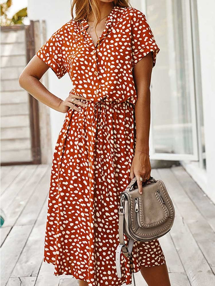Vrouw in oranje-witte stippenjurk met korte mouwen, houdt een beige handtas vast. Zomerse mode, casual dameskleding, trendy jurk.