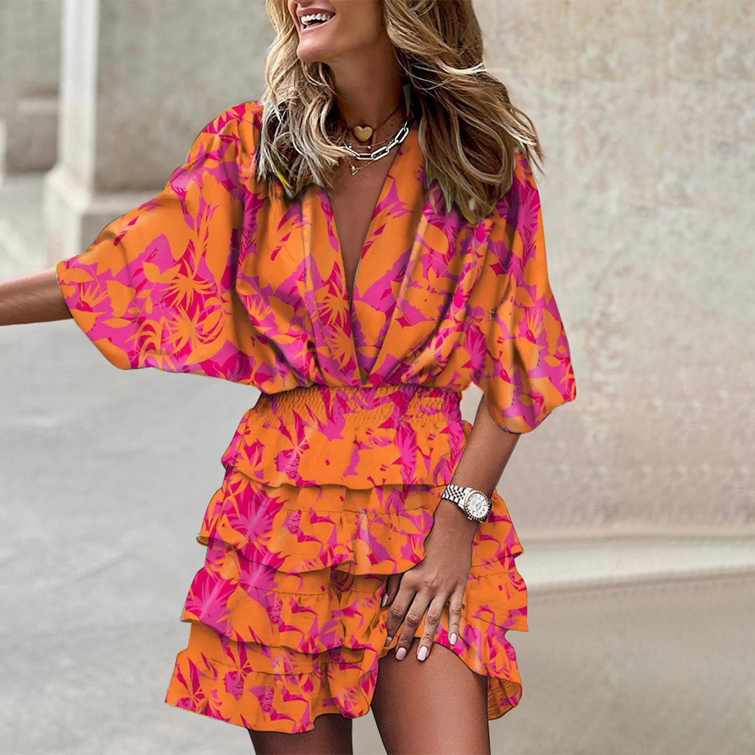 Vrouw in kleurrijke oranje en roze bloemenjurk met ruches, lachend op straat. Trendy zomeroutfit, modieuze dameskleding, casual stijl.