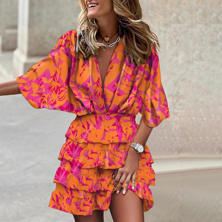Vrouw in kleurrijke oranje en roze bloemenjurk met ruches, lachend op straat. Trendy zomeroutfit, modieuze dameskleding, casual stijl.