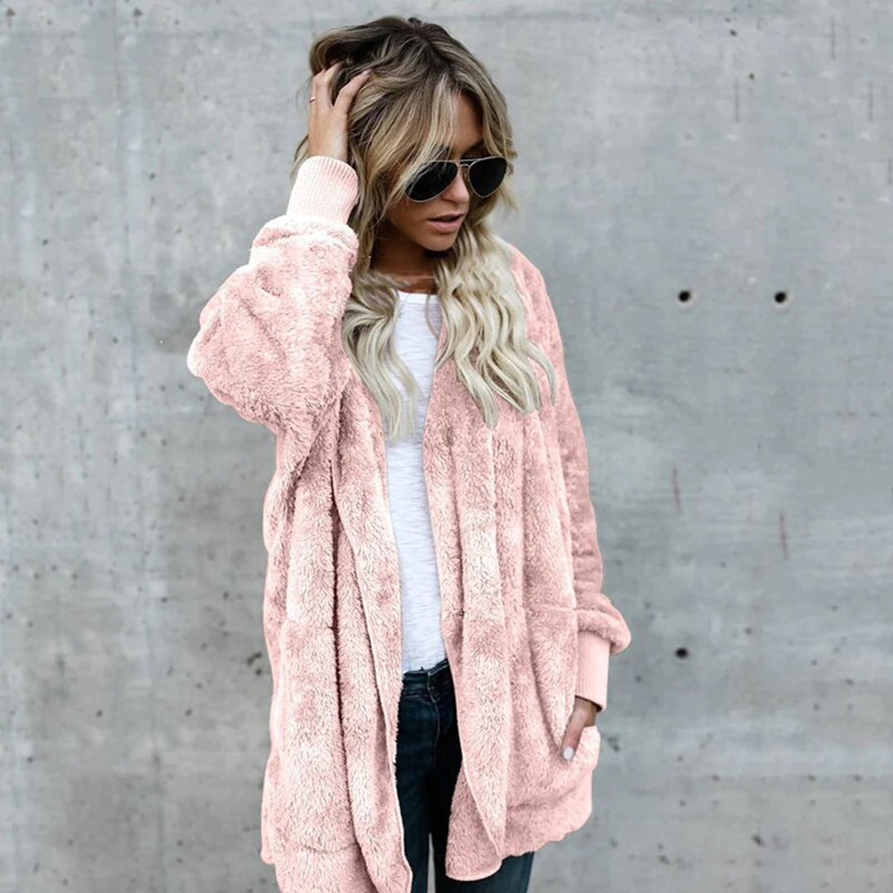 Vrouw in roze teddyjas, witte top en zonnebril tegen betonnen muur. Modieuze dameskleding, herfststijl, casual outfit.