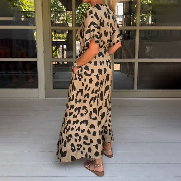 Vrouw in lange luipaardprint jurk op houten veranda, zomermode, casual stijl, comfortabele sandalen, trendy dierenprint, buitenomgeving.