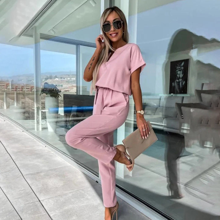 Vrouw in roze jumpsuit met zonnebril en clutch, poseert op modern terras. Stijlvolle damesmode, zomeroutfit, elegante kleding.