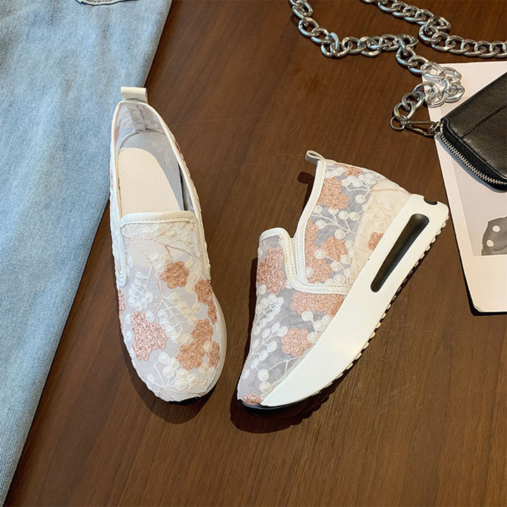 Roze en witte damessneakers met bloemenpatroon, slip-on design en dikke zool, op houten vloer. Trendy casual schoenen voor dagelijks gebruik.