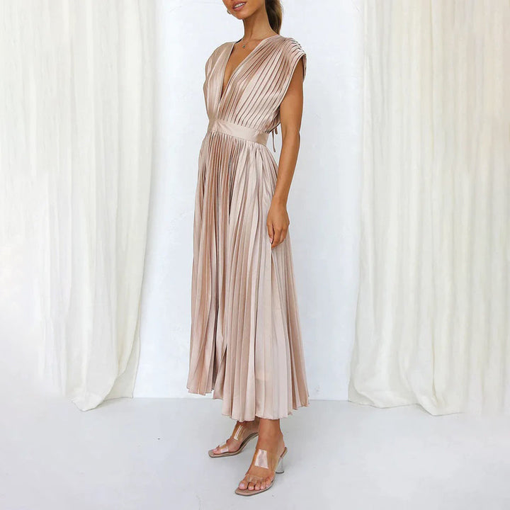 Vrouw in elegante roze geplooide jurk met diepe V-hals, staand voor witte gordijnen. Perfect voor avondkleding, bruiloften, galajurken.