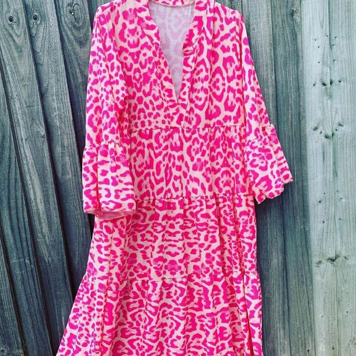 Roze en witte luipaardprint jurk met lange mouwen, V-hals en ruches, hangend tegen een houten achtergrond. Trendy damesmode, opvallende patronen.