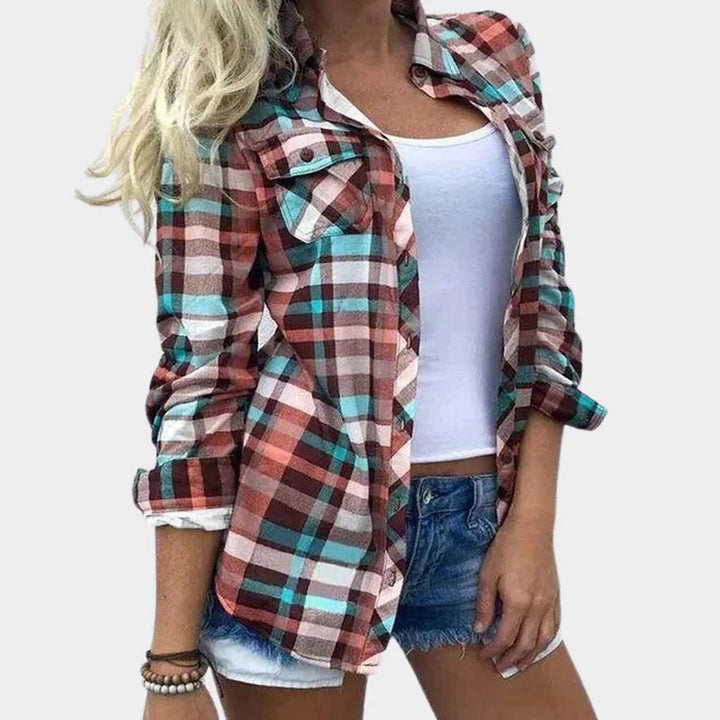 Vrouw in geruite blouse met roze, blauwe en bruine tinten, witte tanktop en denim shorts. Modieuze casual dameskleding.