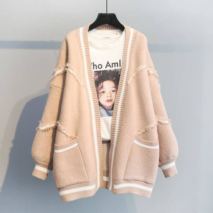 Beige oversized damesvest met zakken, gerafelde details en witte strepen, hangend op een hanger. Trendy en comfortabel herfstkledingstuk.