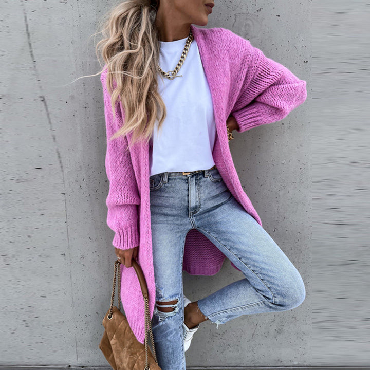 Vrouw in casual outfit met roze gebreid vest, witte T-shirt en gescheurde jeans, poseert tegen een betonnen muur. Modieuze dameskleding, streetwear.