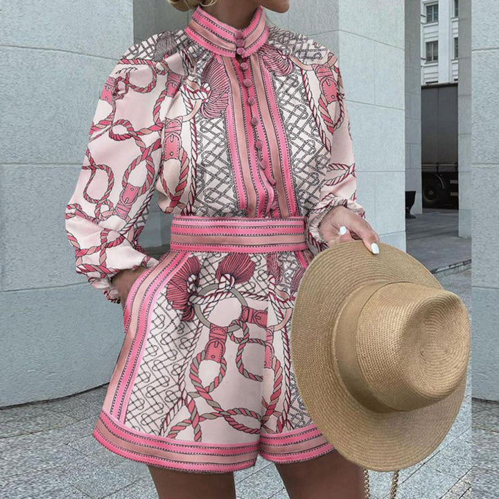 Vrouw in roze en wit geometrisch patroon jumpsuit met lange mouwen, houdt een strohoed vast. Modieuze zomeroutfit, stedelijke achtergrond.