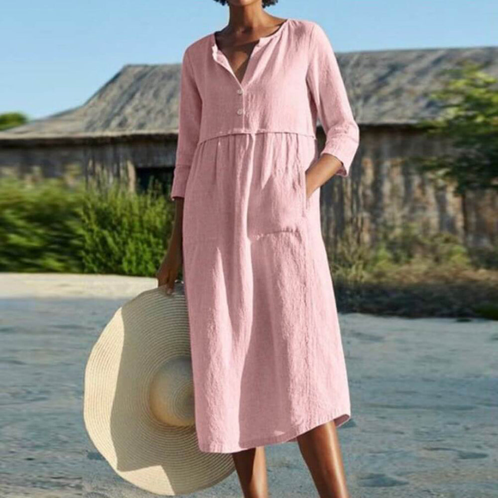 Vrouw in roze linnen jurk met knopen, houdt een grote strohoed vast. Zomerse outfit, casual stijl, buitenomgeving. Perfect voor warme dagen.