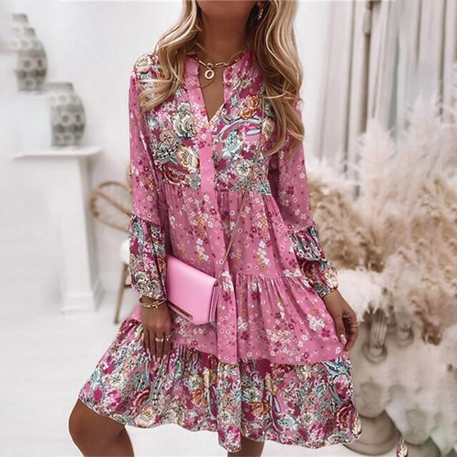 Vrouw in roze bloemenjurk met lange mouwen, houdt roze clutch. Trendy bohemian stijl, perfect voor lente- en zomermode.