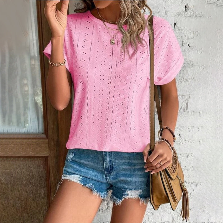 Vrouw in roze geperforeerd T-shirt en denim shorts, met bruine schoudertas. Zomerse mode, casual outfit, trendy dameskleding.