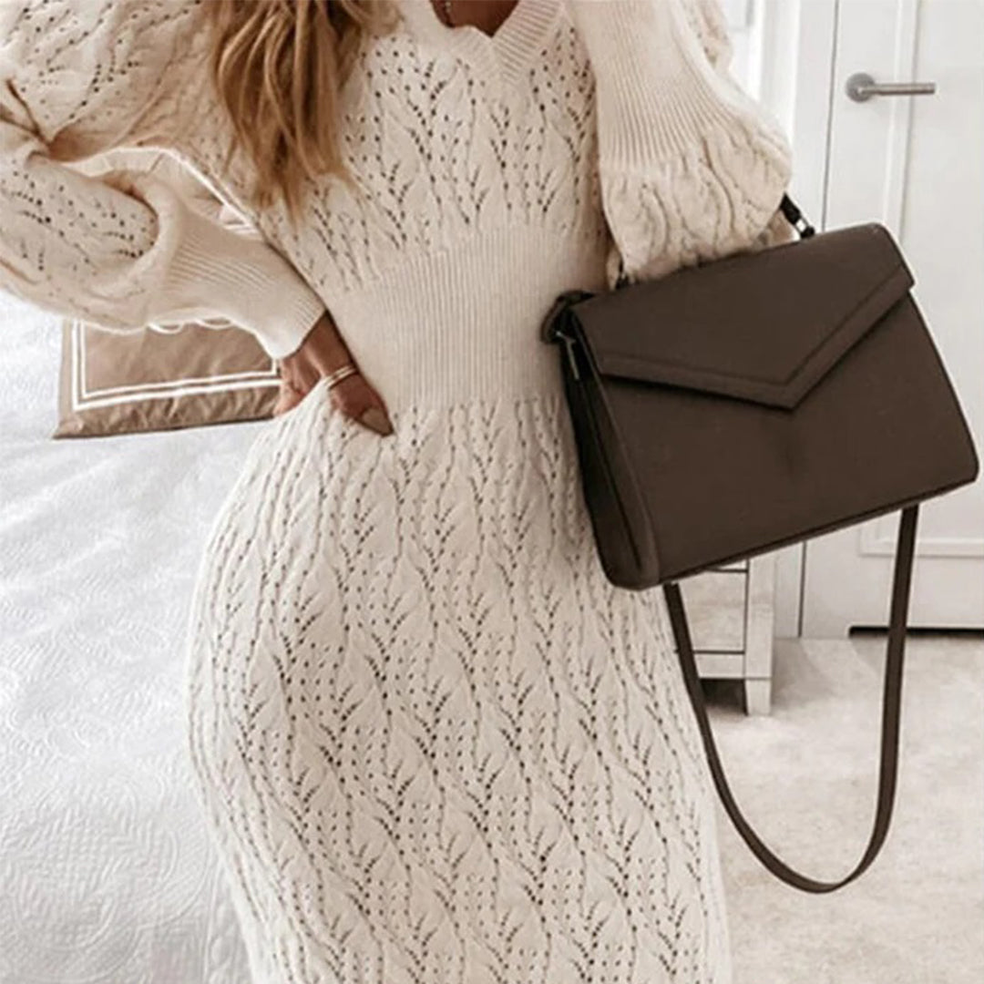 Vrouw in gebreide witte jurk met patroon, draagt een bruine schoudertas. Elegante herfstmode, dameskleding, stijlvolle accessoires.