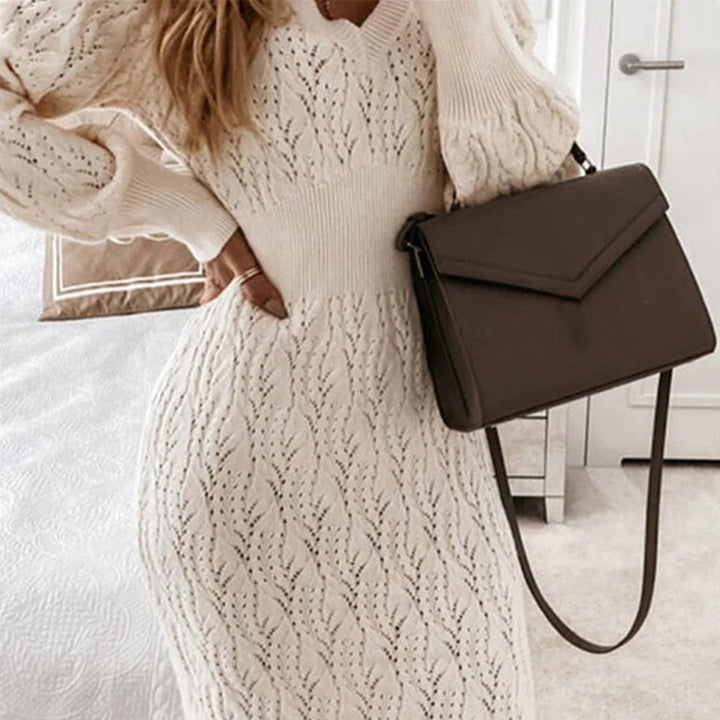 Vrouw in gebreide witte jurk met patroon, draagt een bruine schoudertas. Elegante herfstmode, dameskleding, stijlvolle accessoires.