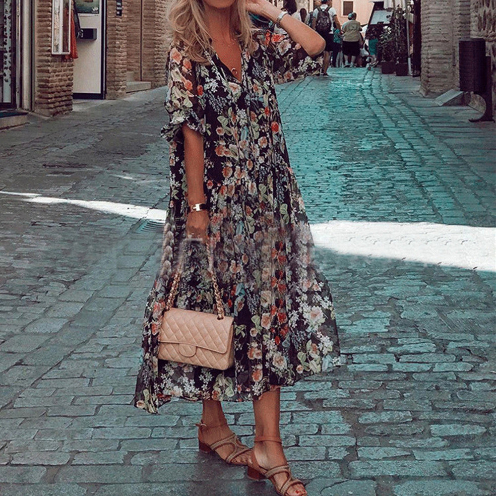 Vrouw in bloemenjurk met beige handtas en sandalen op geplaveide straat. Zomermode, casual outfit, stedelijke achtergrond.