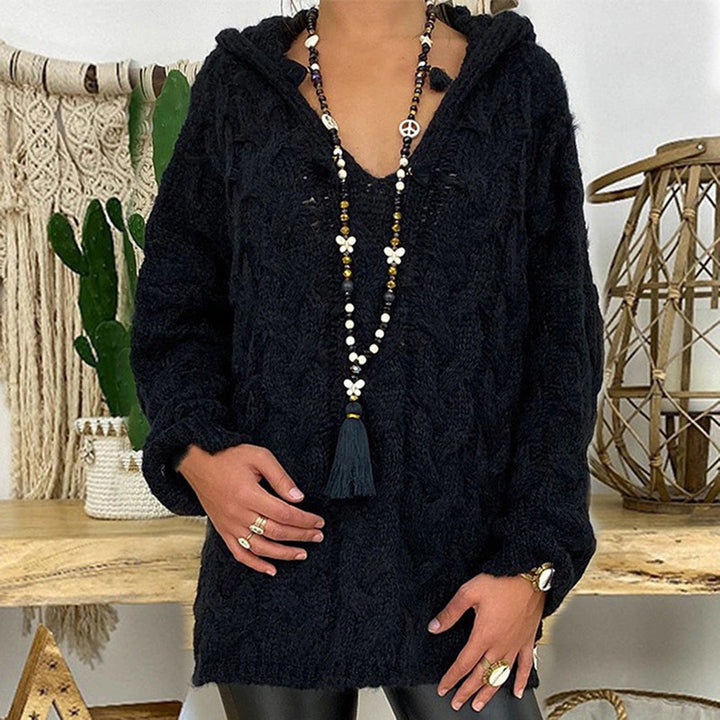Zwarte gebreide trui met capuchon, gedragen door model, gecombineerd met lange kralenketting. Perfect voor herfstmode en casual stijl.