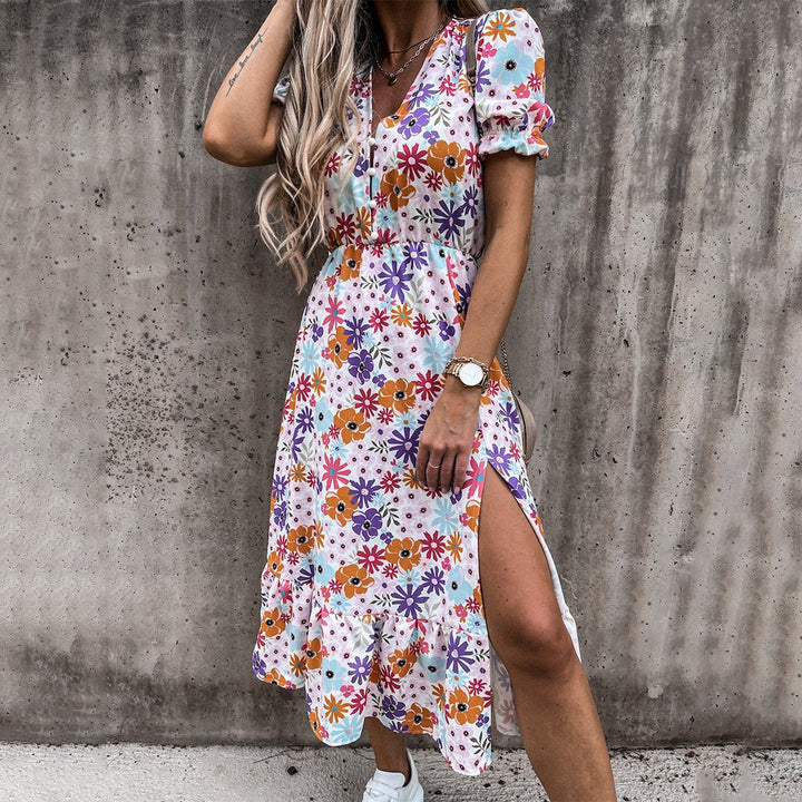 Vrouw in kleurrijke bloemenjurk met korte mouwen en split, poseert tegen betonnen muur. Trendy zomeroutfit, casual stijl, modieuze dameskleding.