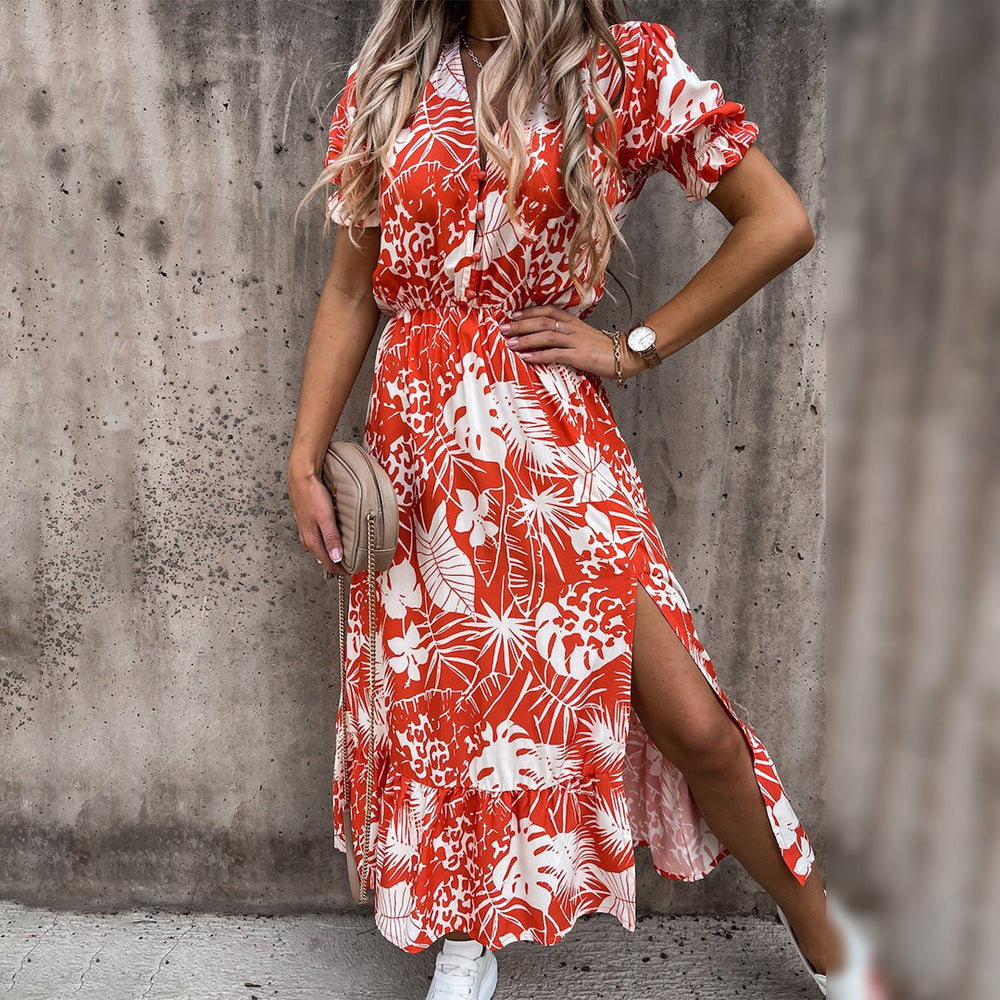 Vrouw in rode bloemenjurk met split, draagt witte sneakers en beige tas. Zomerse mode, casual outfit, trendy dameskleding, stedelijke achtergrond.