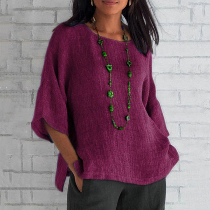 Paarse linnen blouse met driekwart mouwen, gedragen door een vrouw, gecombineerd met een lange groene ketting. Casual damesmode, stijlvolle outfit.