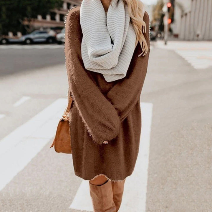 Vrouw in bruine trui jurk met witte sjaal en bruine laarzen op straat. Modieuze herfstoutfit, casual dameskleding, stedelijke achtergrond.