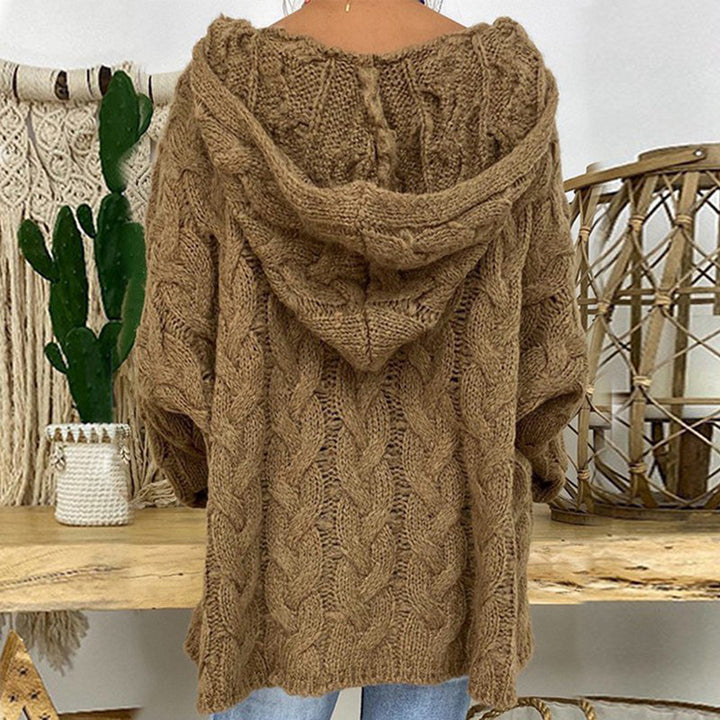 Bruine gebreide oversized trui met kabelpatroon en capuchon, gedragen door model. Perfect voor herfstmode, casual en comfortabel.