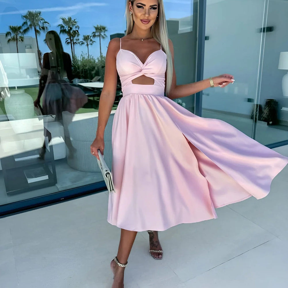 Vrouw in roze zomerjurk met cut-out detail, poseert buiten bij modern huis. Perfect voor zomermode, elegante avondjurk, trendy dameskleding.