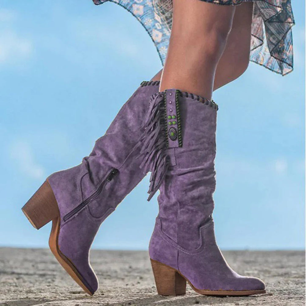 Paarse suède laarzen met hoge hak, franjes en ritssluiting, gedragen door model op zandweg. Trendy damesmode, bohemian stijl.