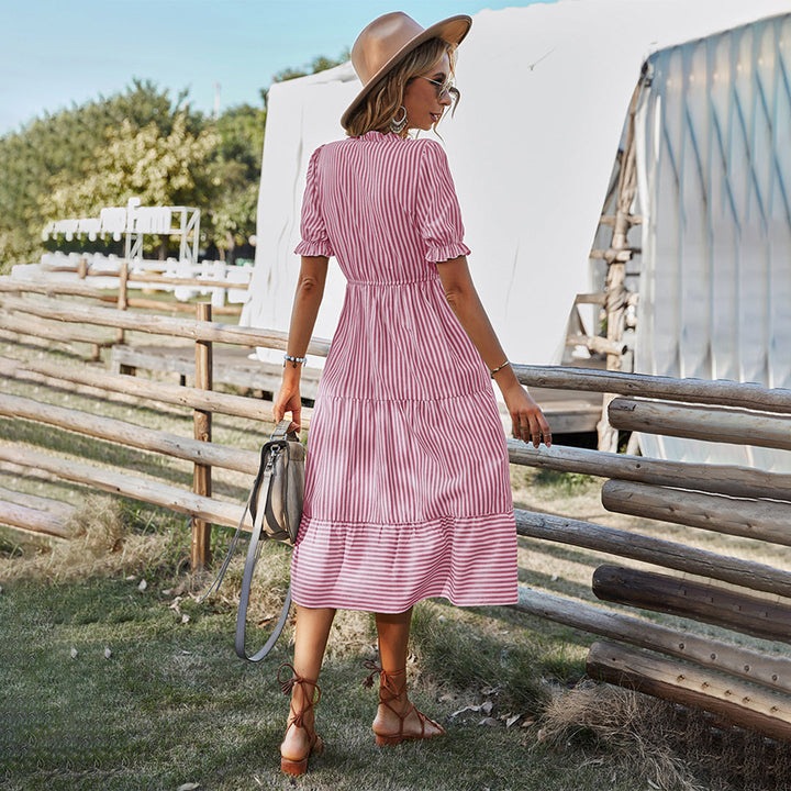 Vrouw in roze gestreepte zomerjurk met hoed en tas, wandelend in een landelijke omgeving. Perfecte outfit voor zomerse dagen.