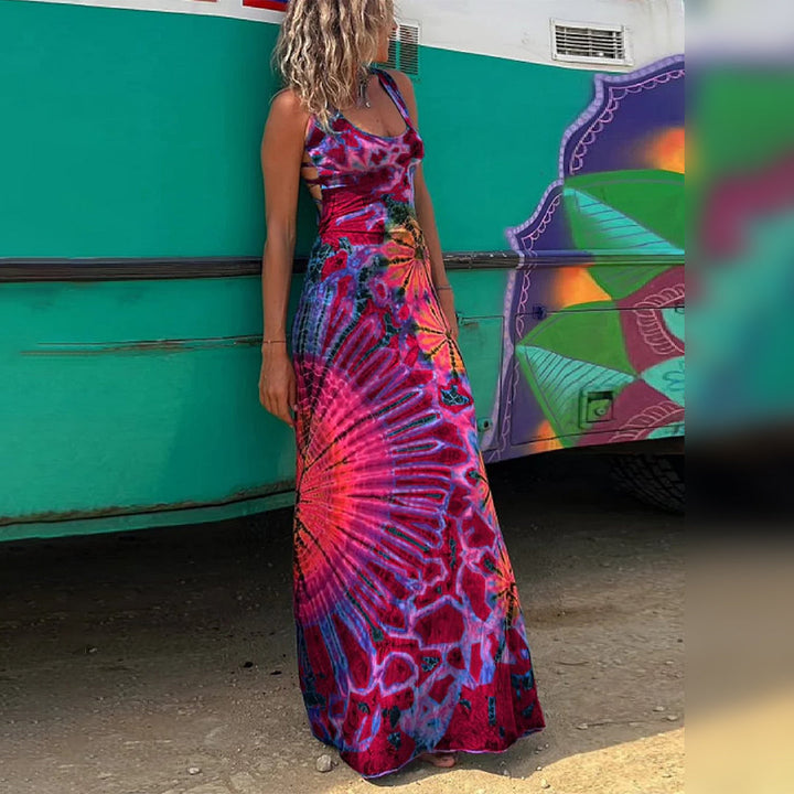 Vrouw in kleurrijke, lange tie-dye jurk met abstract patroon, staand voor een groen voertuig. Zomermode, bohemian stijl, strandkleding.