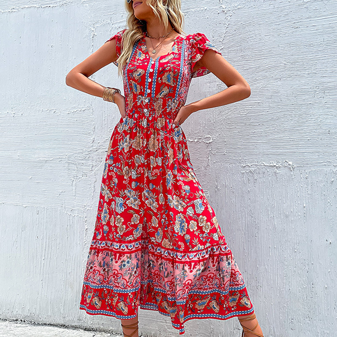 Vrouw in rode bloemenjurk met korte mouwen en bohemian print, poseert tegen witte muur. Zomerse mode, casual stijl, kleurrijke kleding.
