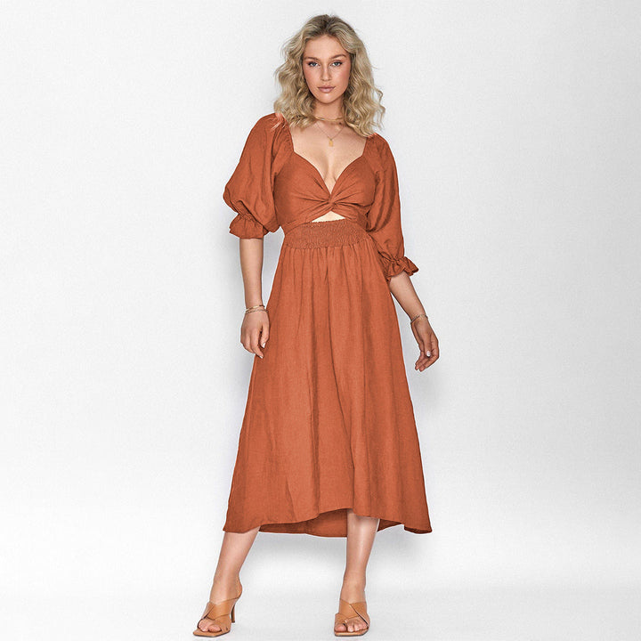 Vrouw in elegante, roestkleurige midi-jurk met pofmouwen en knoopdetail, ideaal voor zomer- en casual gelegenheden. Trendy damesmode.