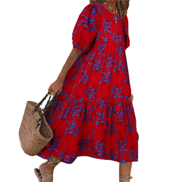 Vrouw in rode bloemenjurk met blauwe accenten, draagt een rieten tas. Zomerse boho-stijl, casual mode, comfortabele pasvorm.