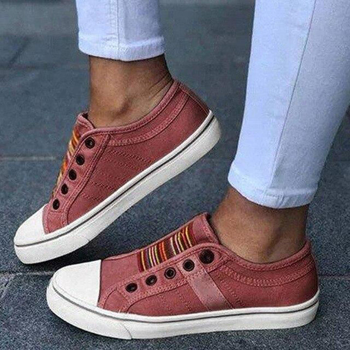 Rode canvas sneakers met witte zolen en kleurrijke strepen, gedragen door persoon in witte broek. Casual schoenen, trendy mode, comfortabele stijl.