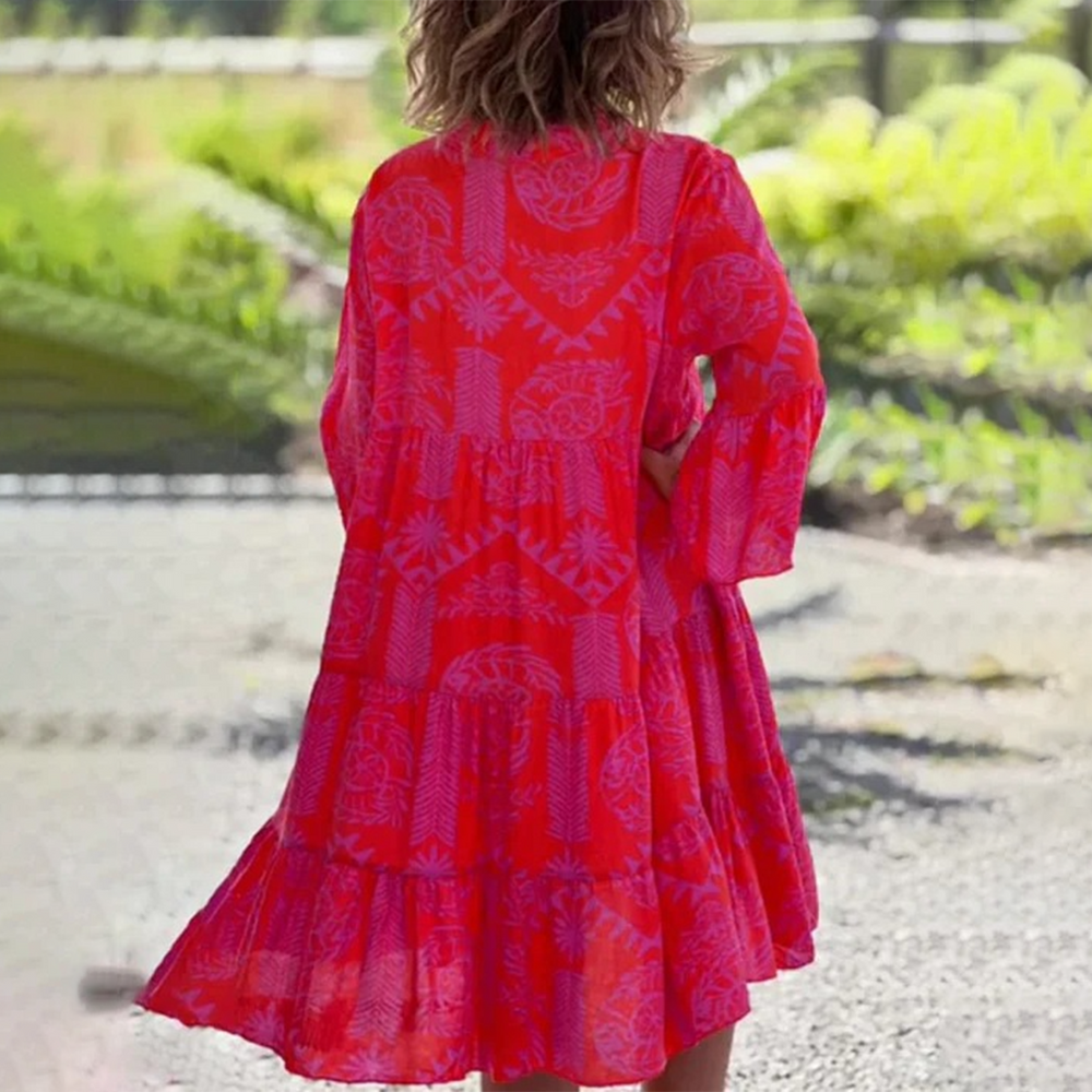 Vrouw in felrode boho-jurk met paisley-patroon, buiten in groene omgeving. Zomerse mode, casual stijl, kleurrijke kleding.