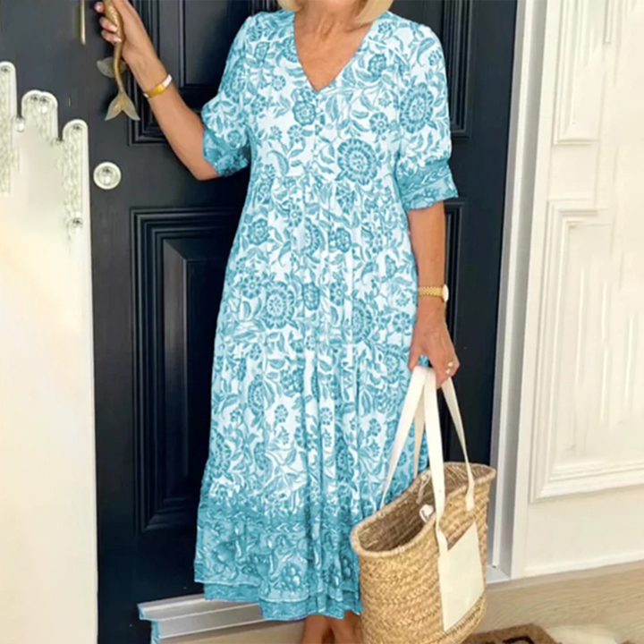 Vrouw in blauwe bloemenjurk met rieten tas voor zwarte deur. Zomerse outfit, casual stijl, modieuze dameskleding, comfortabele pasvorm.