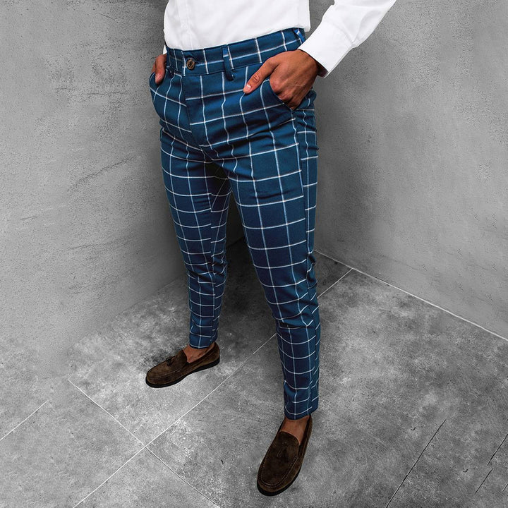 Man in blauwe geruite broek, witte overhemd, bruine loafers, grijze achtergrond. Stijlvolle herenmode, casual outfit, trendy kleding.