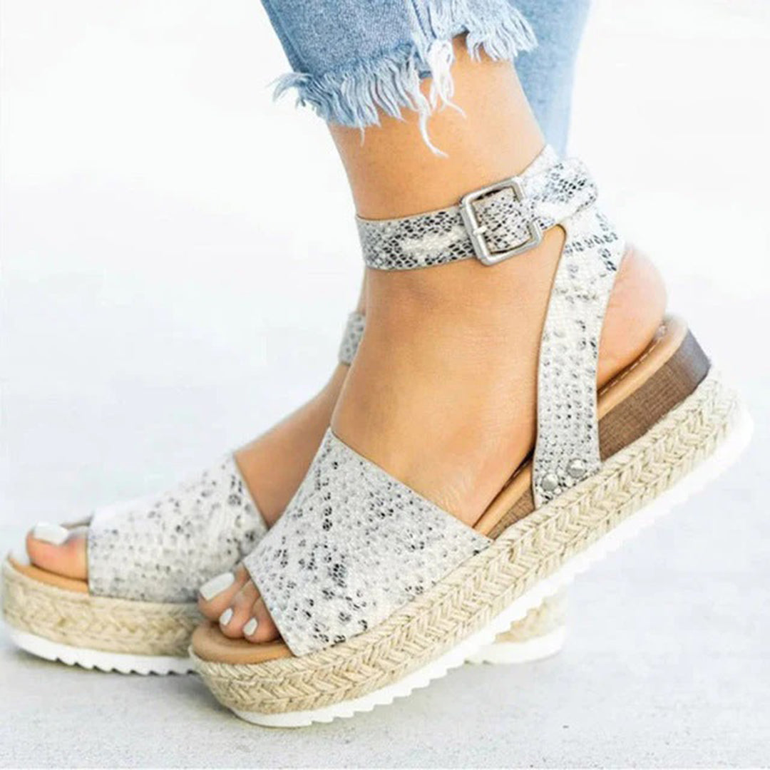 Vrouw draagt modieuze slangenleren sandalen met sleehak en gesp, gecombineerd met gerafelde jeans. Perfect voor zomerse casual outfits.