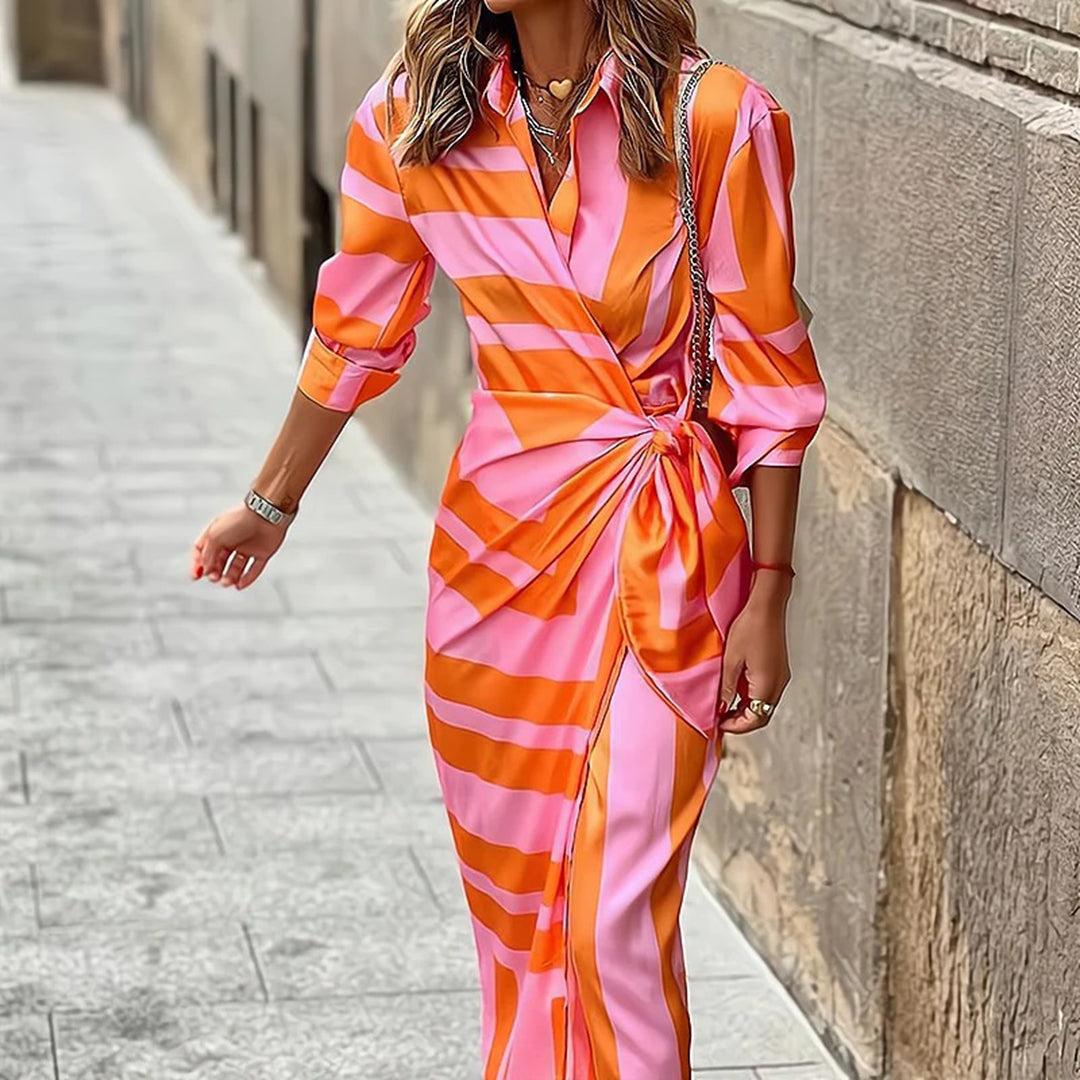 Stijlvolle zomerjurk met roze en oranje strepen, knoopdetail, driekwart mouwen. Perfect voor modieuze zomerdagen. Vrouw loopt op straat.