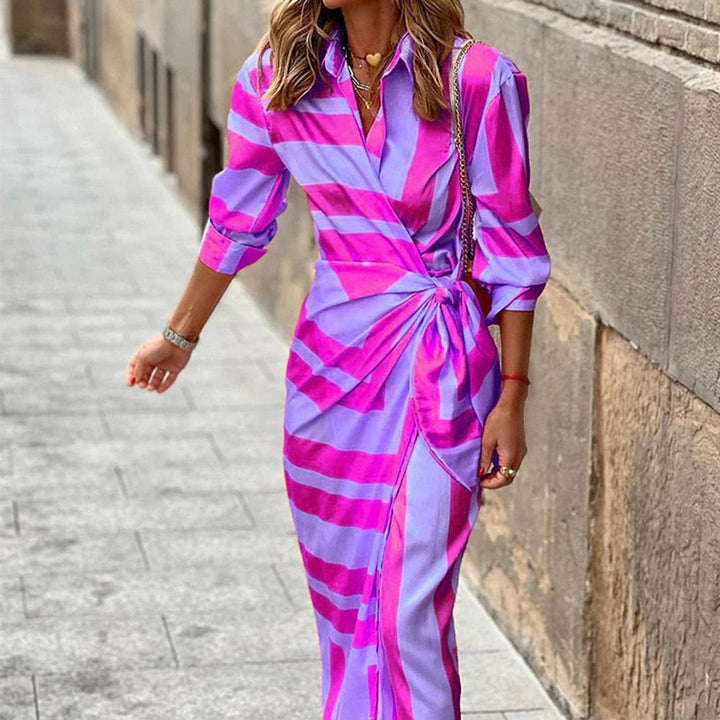 Stijlvolle roze en paarse zomerjurk met strepen, lange mouwen en strikdetail, gedragen door vrouw op straat. Perfect voor modieuze zomerdagen.