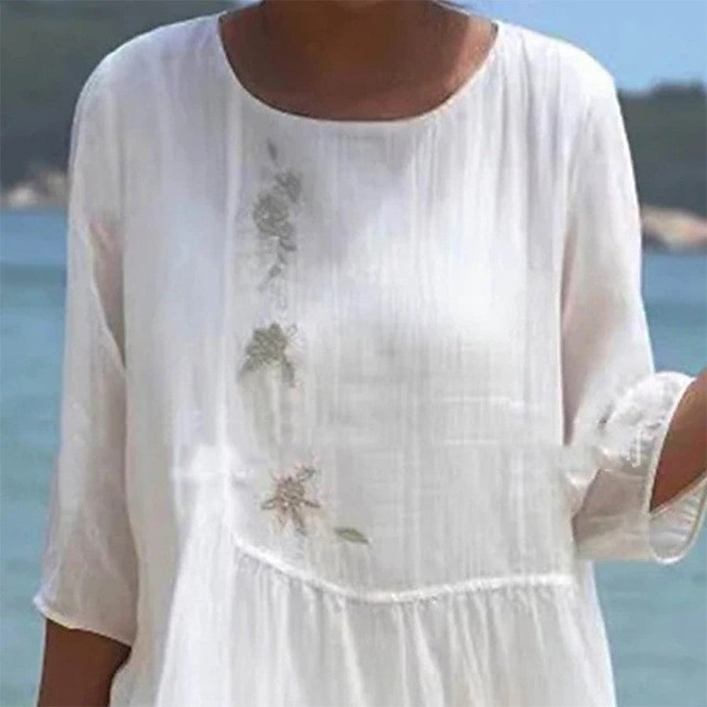 Witte linnen tuniek met bloemenborduursel, driekwart mouwen, strandachtergrond. Perfect voor zomermode en casual strandkleding.