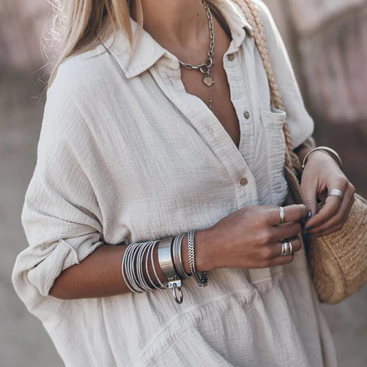 Vrouw in witte linnen blouse met zilveren sieraden en rieten tas. Trendy zomeroutfit, casual mode, boho stijl. Perfect voor warme dagen.