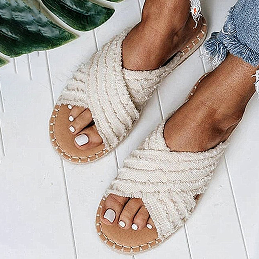 Witte, geweven dames sandalen met kruisbanden, gedragen op een witte houten vloer. Perfect voor zomerse outfits en casual stijl.