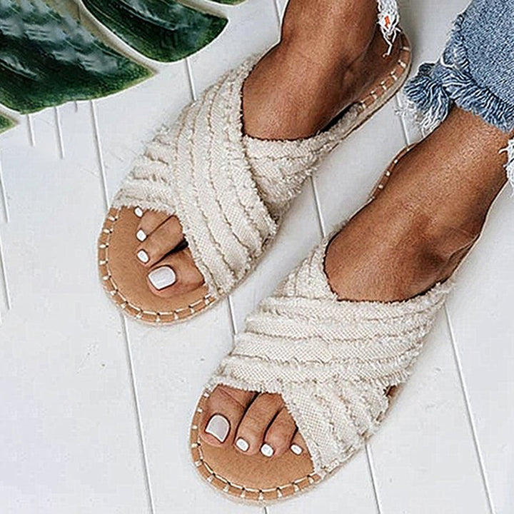 Witte, geweven dames sandalen met kruisbanden, gedragen op een witte houten vloer. Perfect voor zomerse outfits en casual stijl.