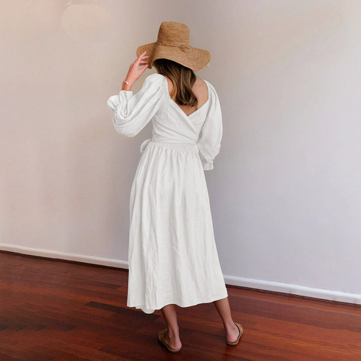 Vrouw in witte zomerjurk met lange mouwen en strohoed, staand op houten vloer. Ideaal voor casual lente- en zomermode.
