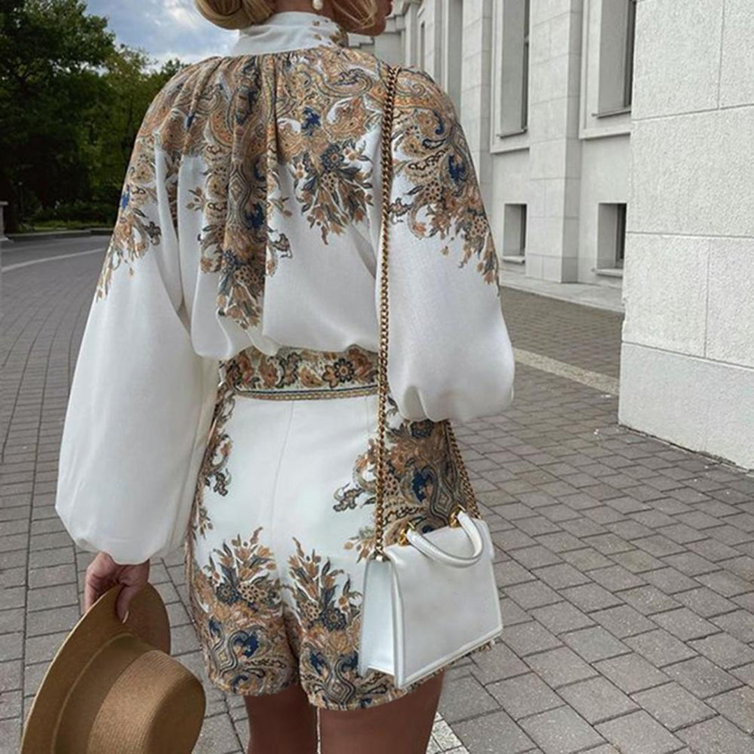 Vrouw in elegante witte jurk met barokke print, draagt een witte handtas en hoed, loopt op een geplaveide straat. Zomeroutfit, modetrend 2023.