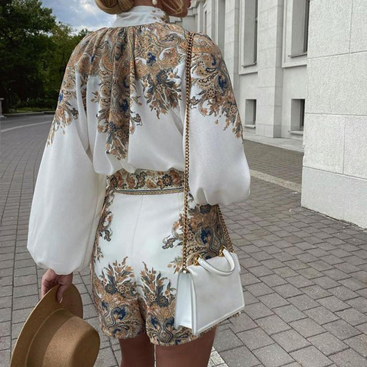 Vrouw in elegante witte jurk met barokke print, draagt een witte handtas en hoed, loopt op een geplaveide straat. Zomeroutfit, modetrend 2023.